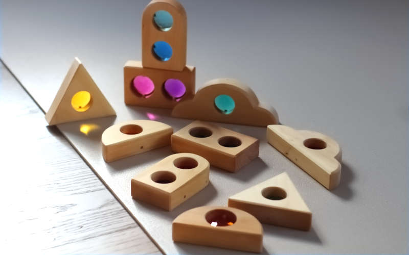 BAUSPIEL Märchenfenster Holzbausteine mit bunten Acrylsteinen als Fensterelemente, die schöne Lichtreflektionen und -effekte erzeugen.
